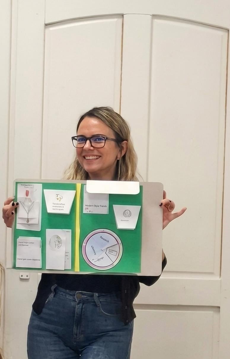 Cristina Ciungu prezentând un lapbook didactic colorat, cu fișe și o roată de cercetare, în fața unei uși albe